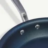 A close-up of a non-stick frying pan with a metallic handle, showcasing the interior rivets and speckled surface.