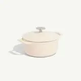 A cream-colored dutch oven with a lid is positioned center on a light background.