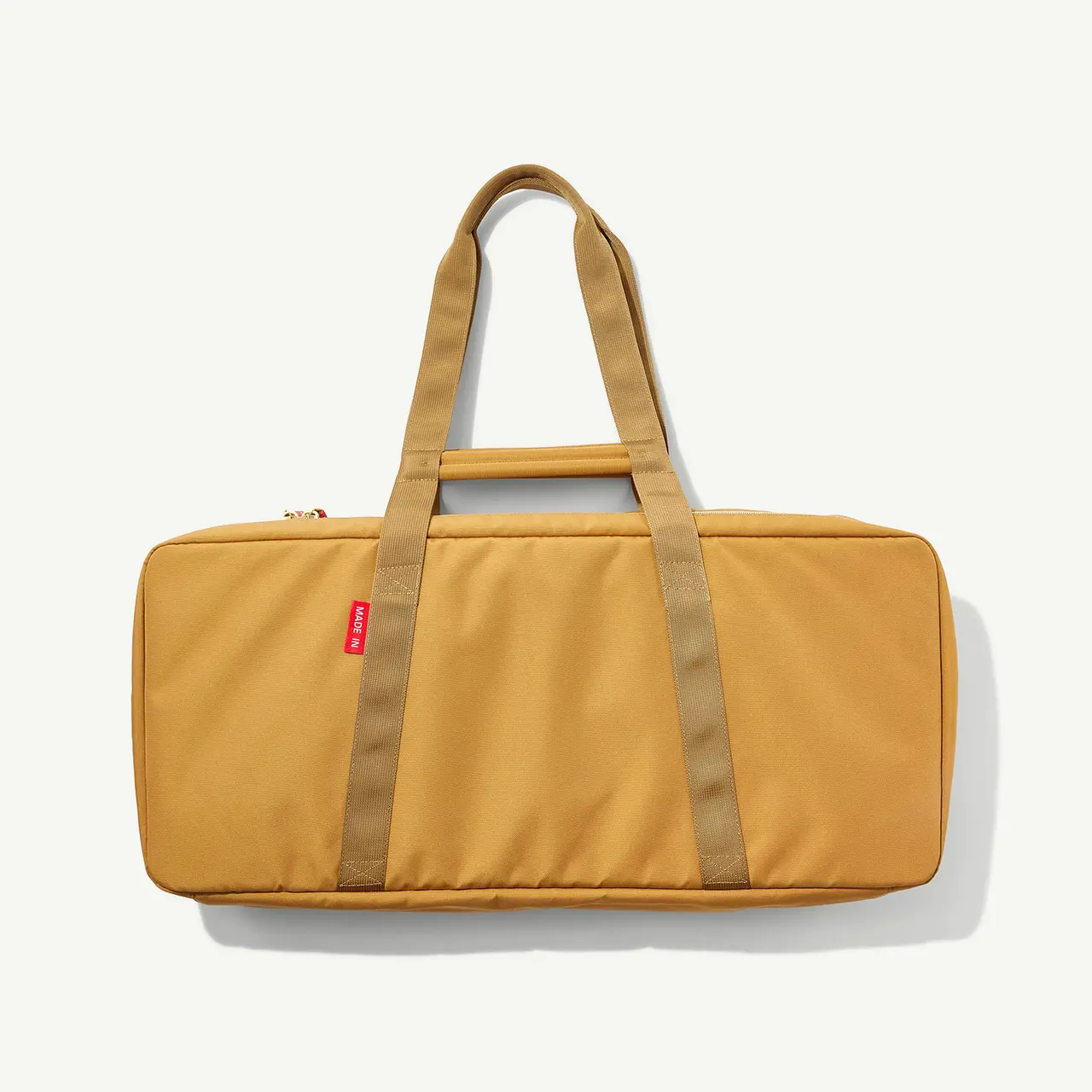 A mustard yellow duffel bag with two handles and a brand label on a light background.