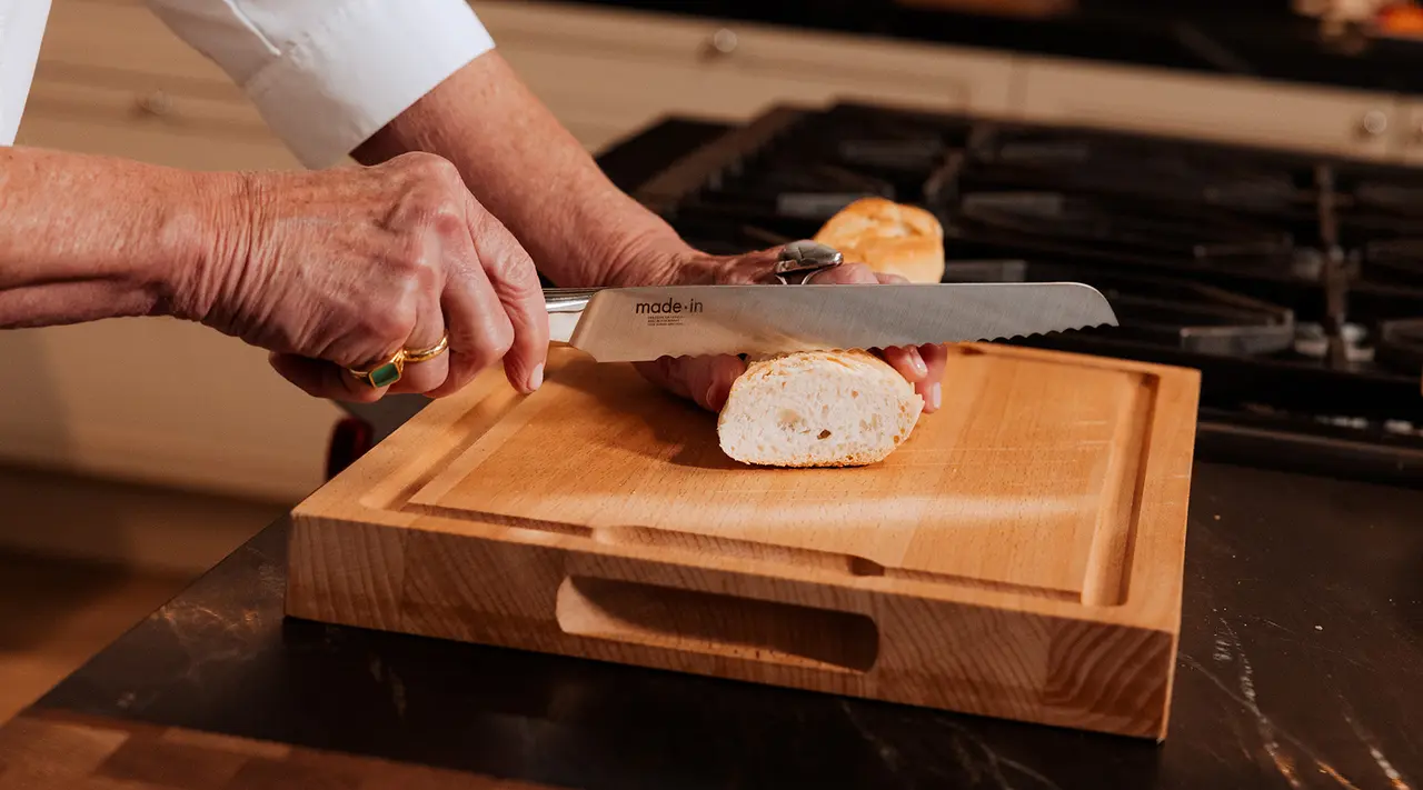 A person is slicing a loaf of bread on a wooden cutting board in a kitchen.