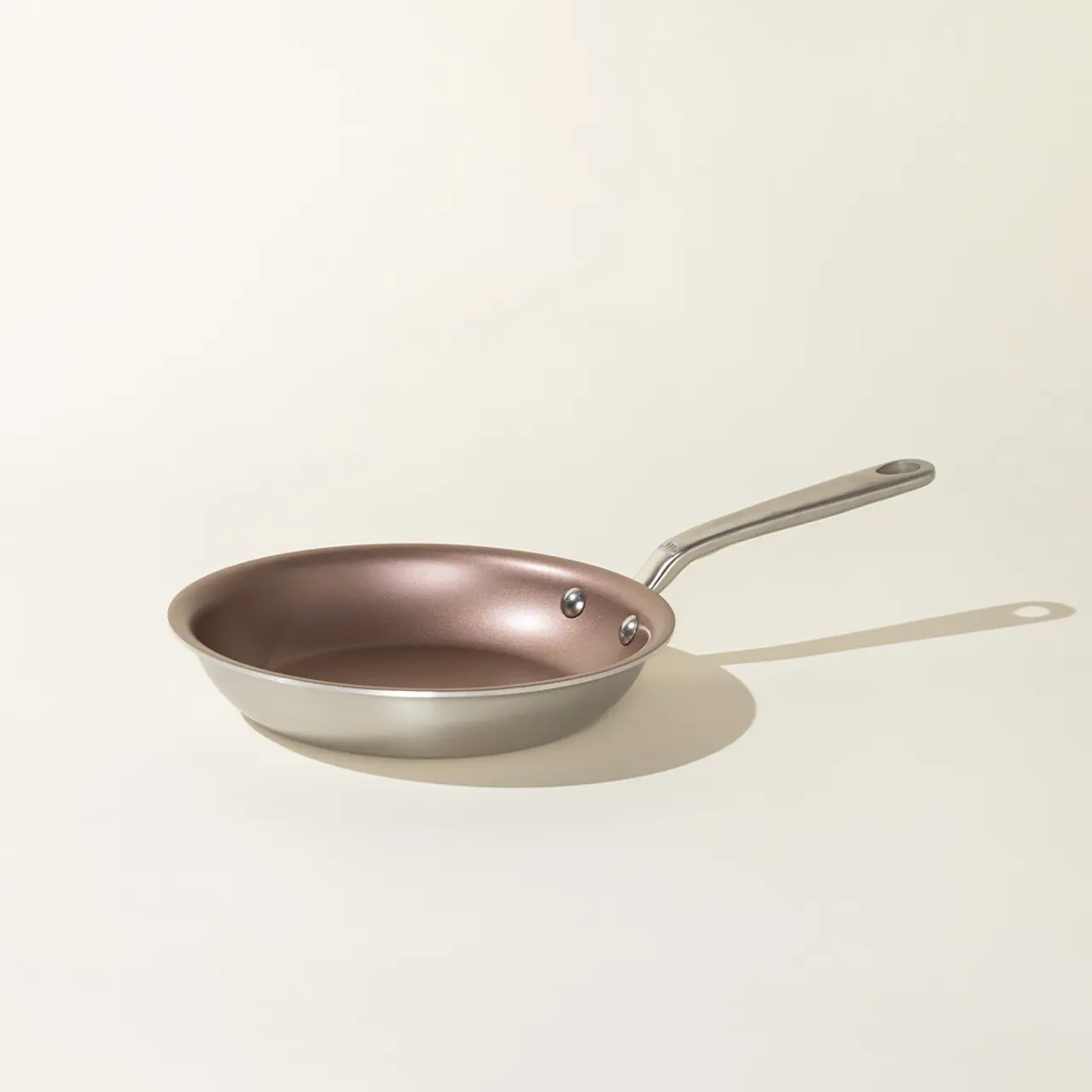 A copper-colored frying pan with a silver handle lies against a neutral background.