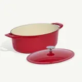 A red enameled cast iron Dutch oven with its lid placed to the side sits against a white background.