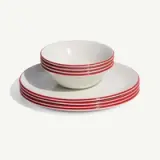A stack of clean white dishes with red stripes includes two plates and a bowl on a white background.