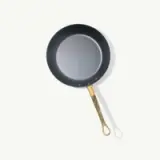 A sleek black frying pan with a gold-toned handle is centered against a light background.