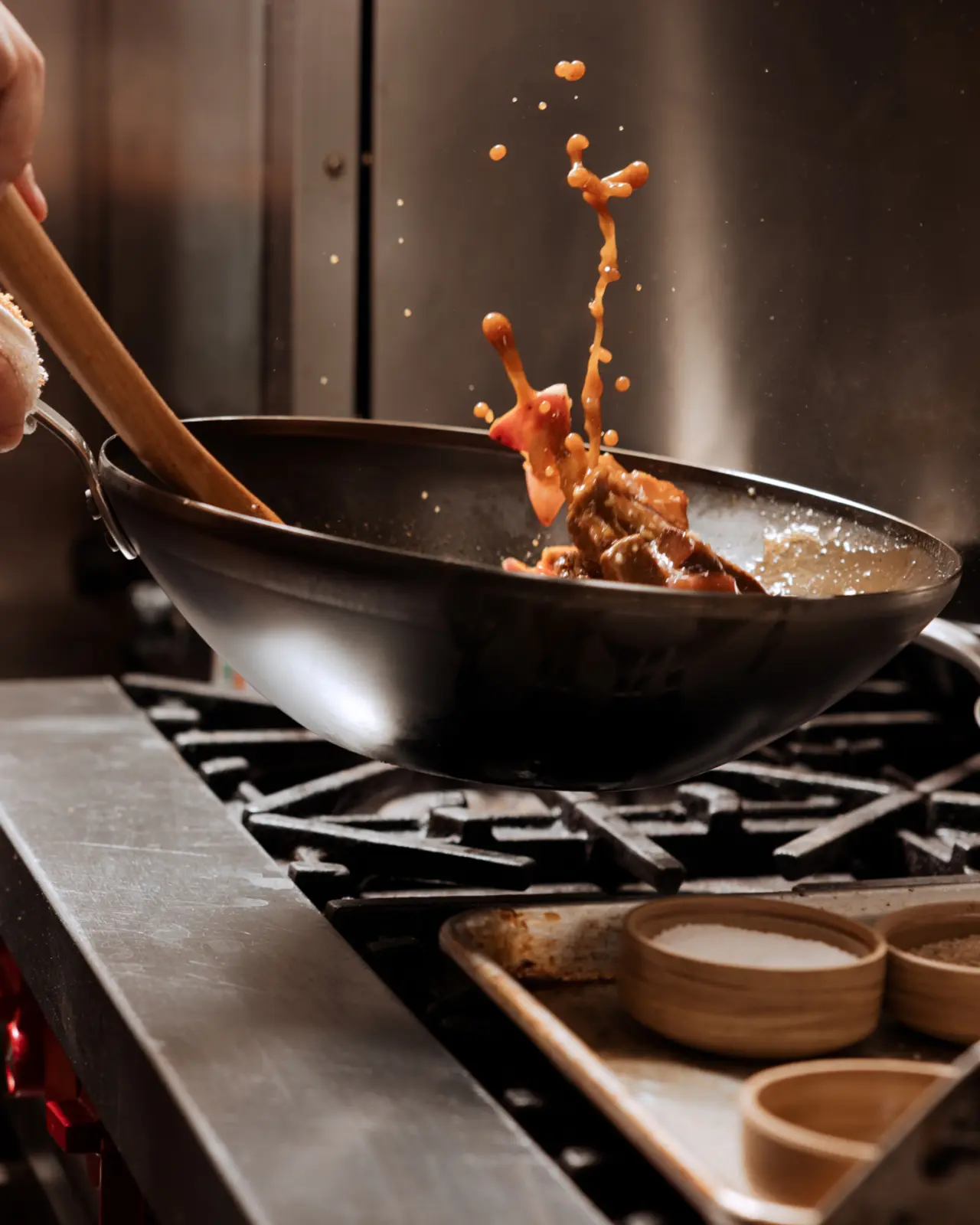 Stir-fried food sizzles as it leaps from a wok above a gas stove, with splashes of sauce captured in mid-air.