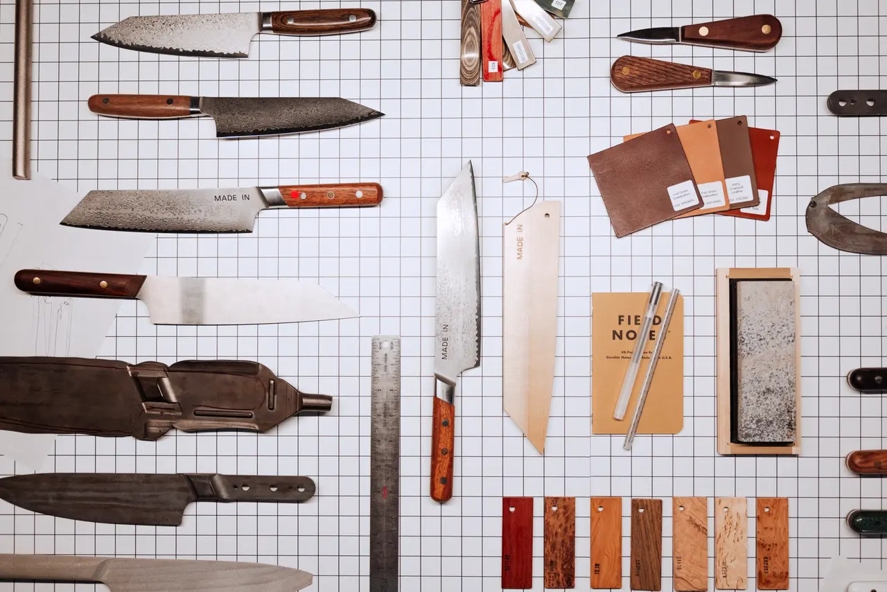 Various knives and leather sheaths are meticulously arranged on a gridded background, creating an orderly display.