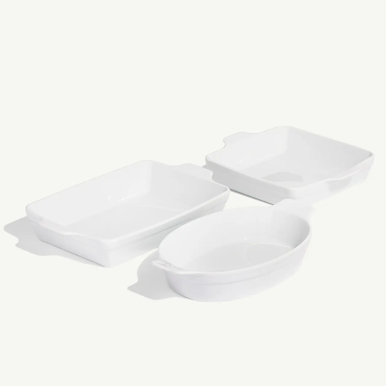 Three white baking dishes in varying shapes and sizes are arranged on a light background.
