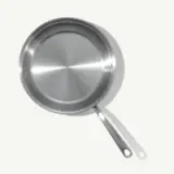 A stainless steel frying pan is shown from above with its handle extending to the left against a light background.
