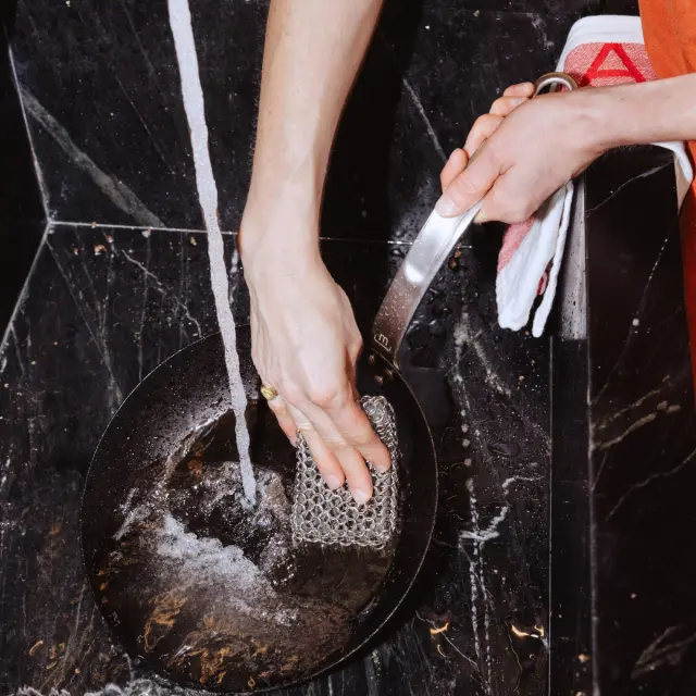 A hand using a sponge to wash a dark bowl under running water.