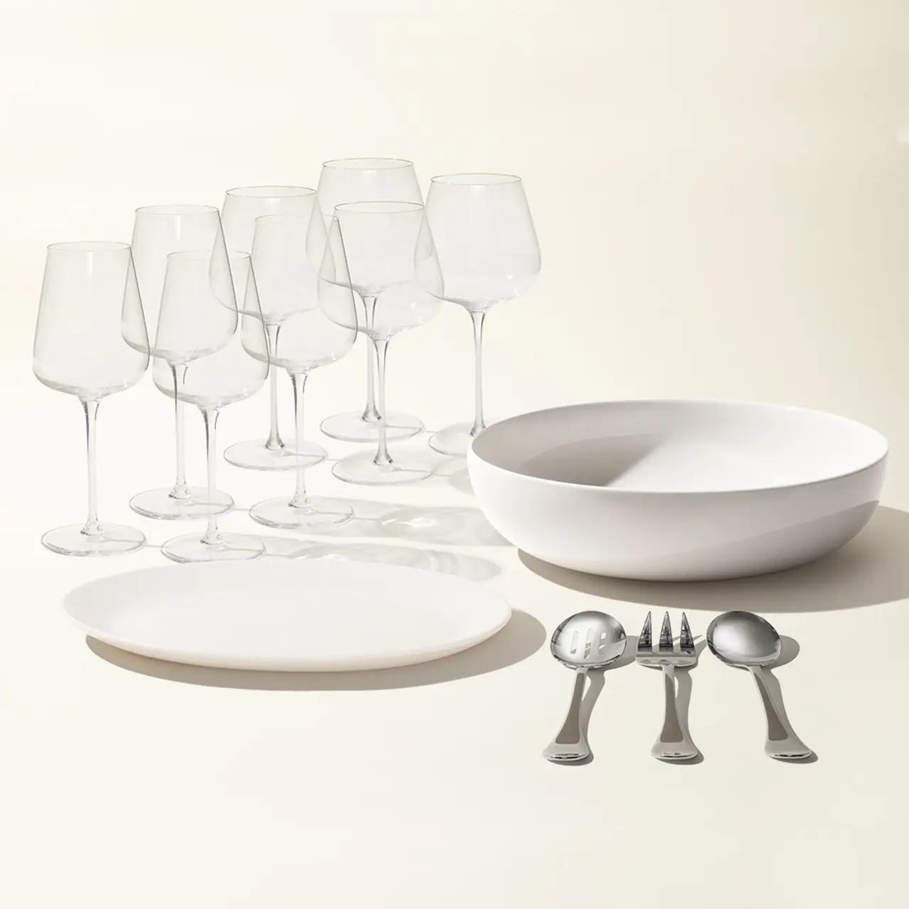 A collection of dining ware including plates, bowls, an assortment of glasses, and silverware is arranged neatly against a light background.