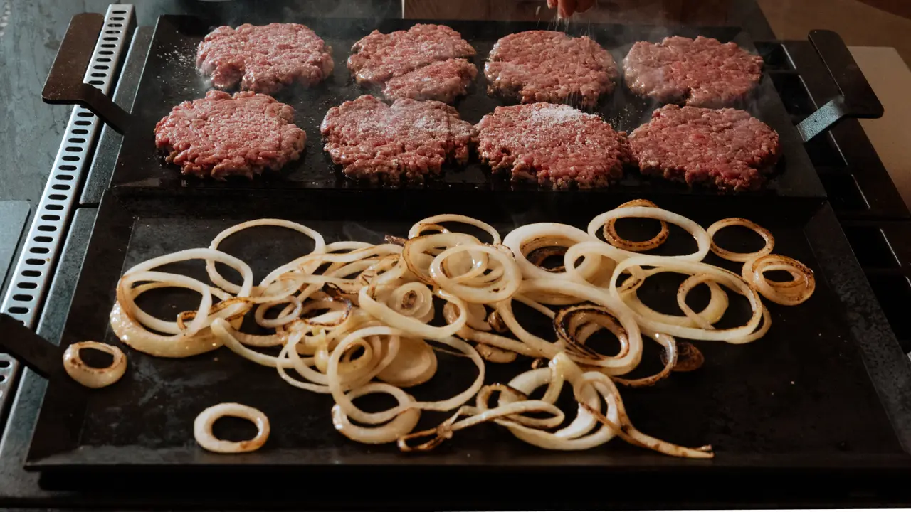 Hamburgers and onion rings are being grilled on a stovetop griddle.