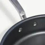 A close-up view of a non-stick frying pan with two water droplets inside and a visible handle.
