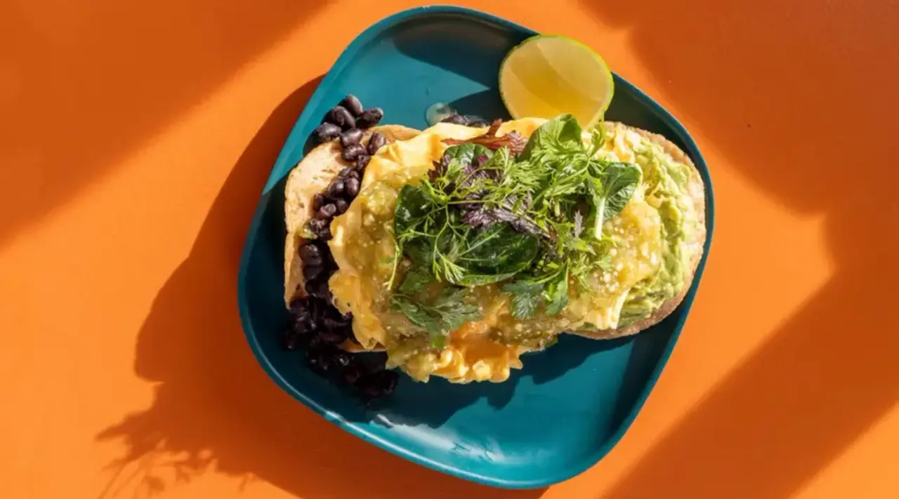 A plate of scrambled eggs topped with fresh herbs, a side of black beans, and a lime wedge on a teal plate against an orange backdrop.