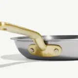 A close-up of a stainless steel frying pan with a gold-colored handle displaying the branding "made in."