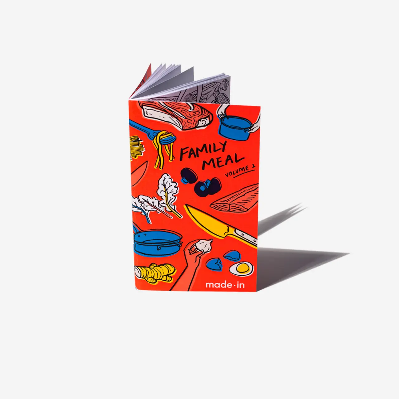 A vibrant red cookbook titled "FAMILY MEAL" with various food illustrations on its cover stands upright against a white background with a prominent shadow to the right.