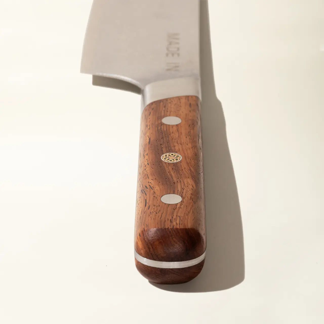 A close-up of a chef's knife with a wooden handle resting on a light surface, highlighting its blade and brand stamp.