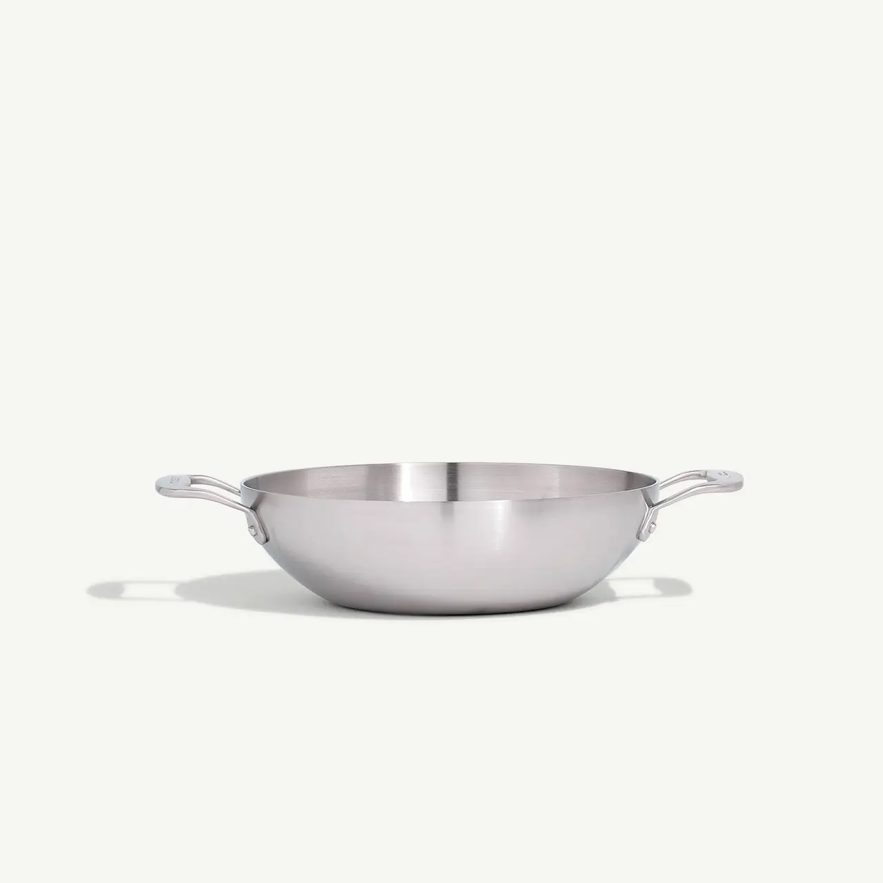 A stainless steel frying pan with two handles is centered on a light background.