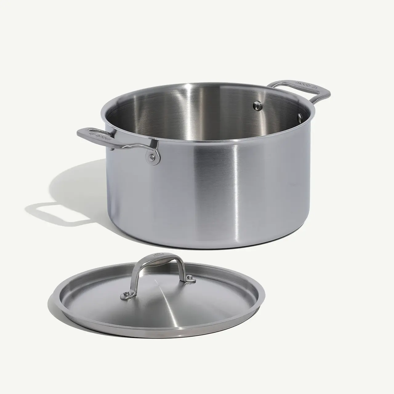 A stainless steel cooking pot with its lid off to the side on a neutral background.