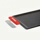A black griddle with a red silicone handle on one side.