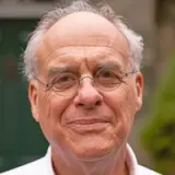 A close-up photo of an elderly man with glasses and a gentle smile on his face.