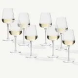 Eight elegant wine glasses filled with white wine are arranged in a neat row, casting soft shadows on a light background.