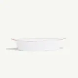 A white oval baking dish with a red rim sits isolated against a light background.