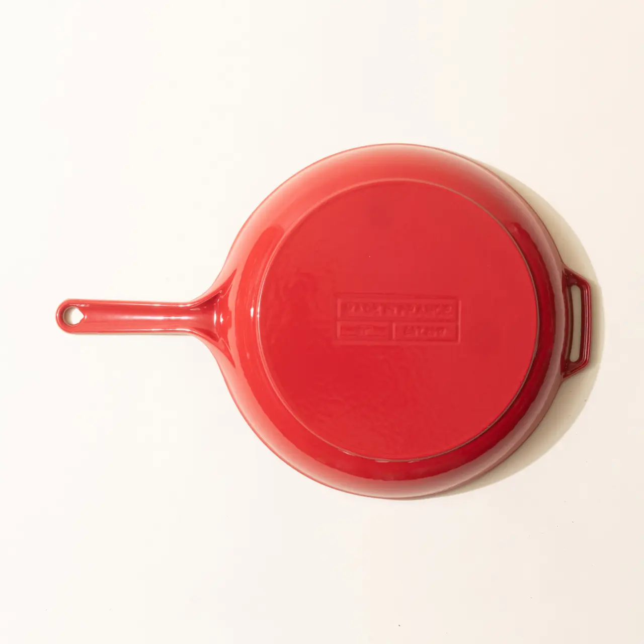 A red enameled cast iron skillet is positioned on a white surface.