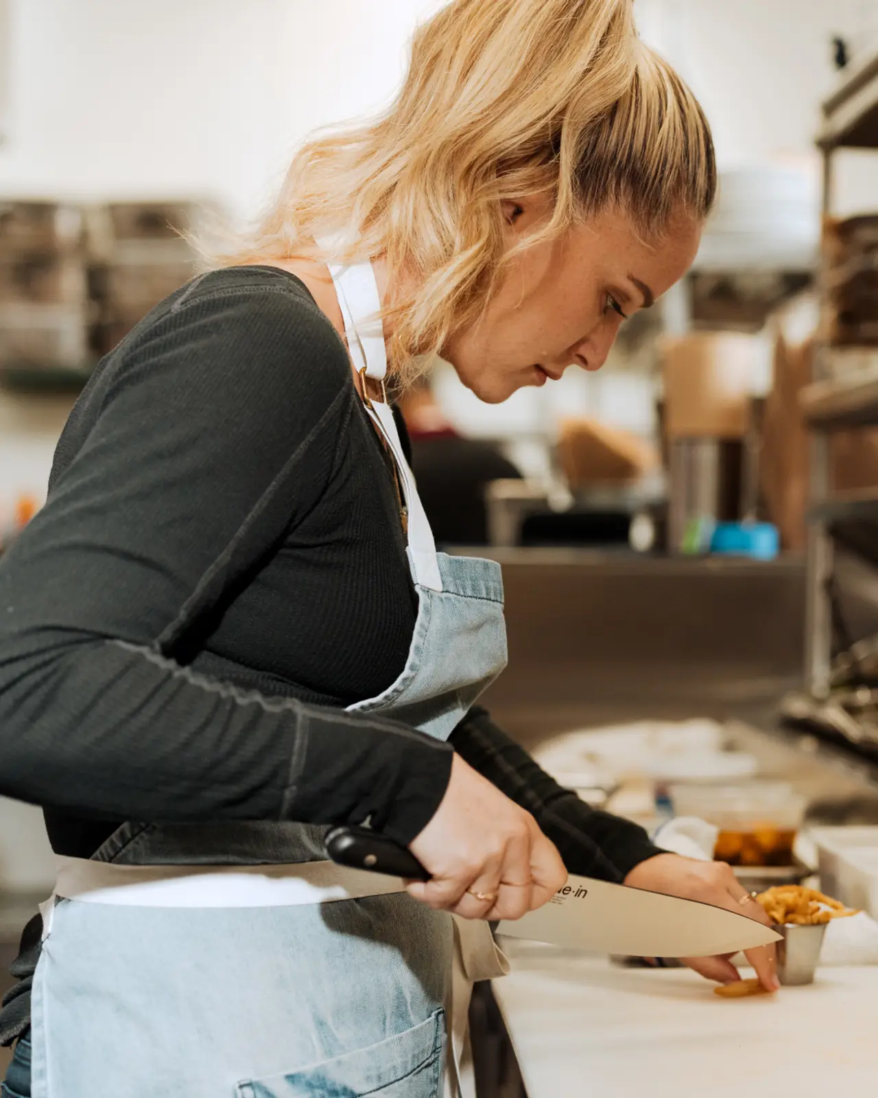 A focused person wearing an apron is cutting food in a commercial kitchen setting.