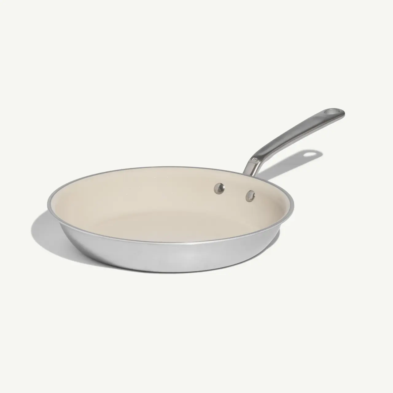 A stainless steel frying pan with a cream-colored non-stick interior and a silver handle sits against a light background.