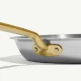 A stainless steel frying pan with a gold-colored handle against a light background.
