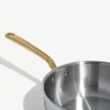 A stainless steel pot with a gold-colored handle sits on a light background.