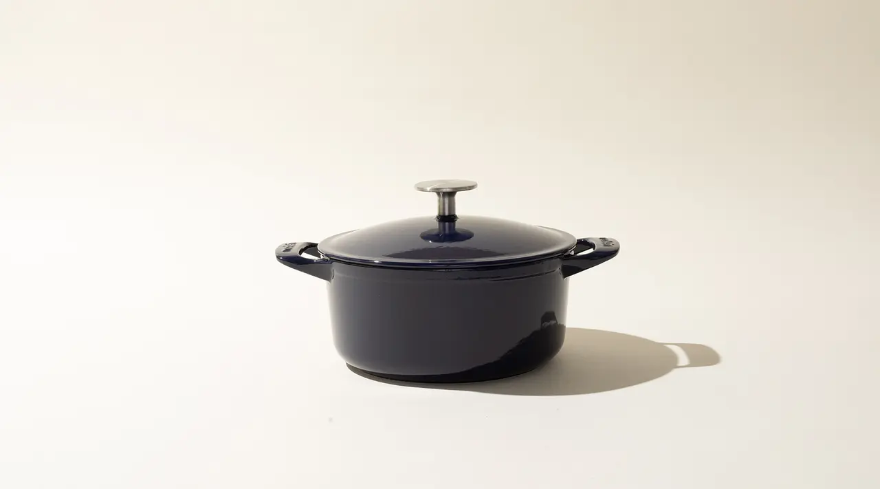 A black cast iron Dutch oven with a lid on a light background.