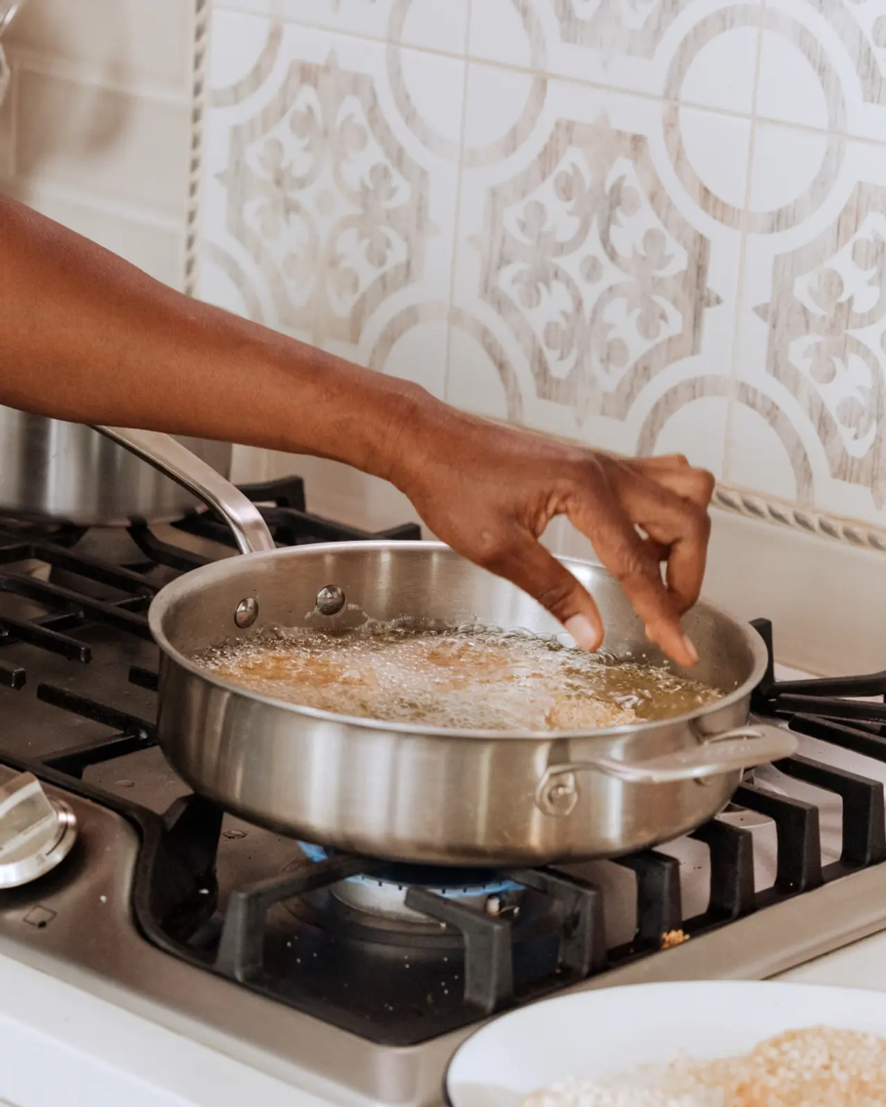 A person's hands are seen frying food in a stainless steel pan on a gas stove.