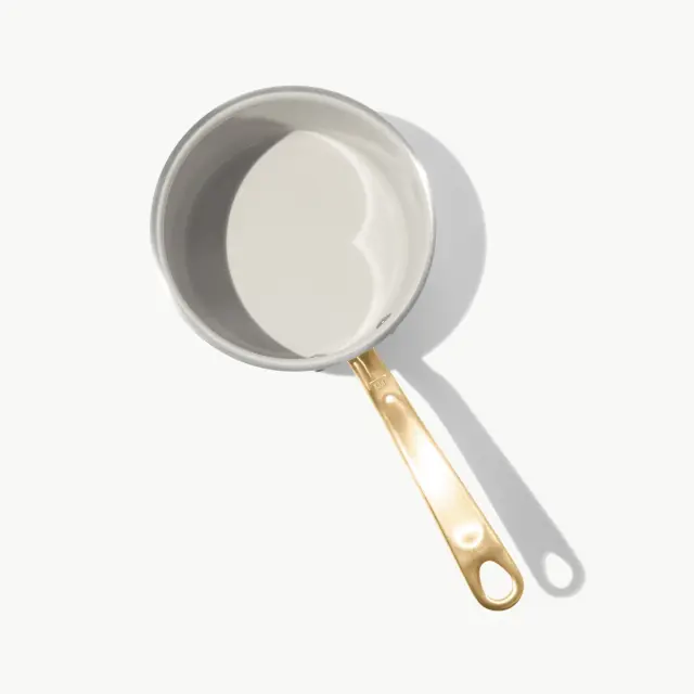 A round cooking pot with a shiny metallic finish and a golden handle, casting a shadow on a light background.