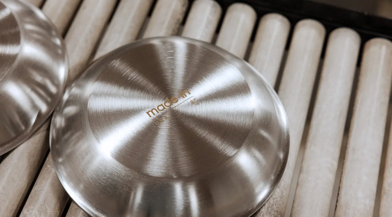 A close-up of two stainless steel lids with a concentric pattern on a textured surface.