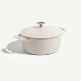 A light-colored cooking pot with a lid and side handles sits on a neutral background, casting a soft shadow.