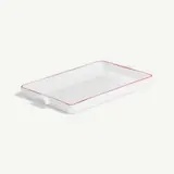 A white rectangular ceramic baking dish with red trim on a plain background.