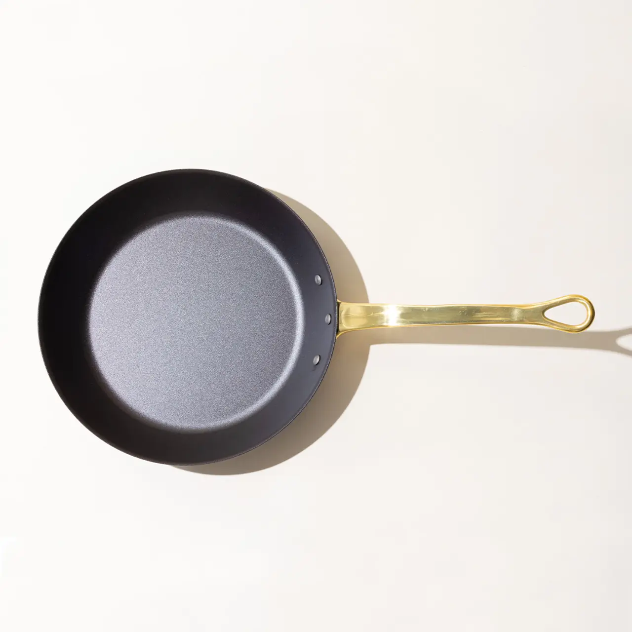 A nonstick frying pan with a gold-colored handle on a plain, light background, casting a slight shadow.