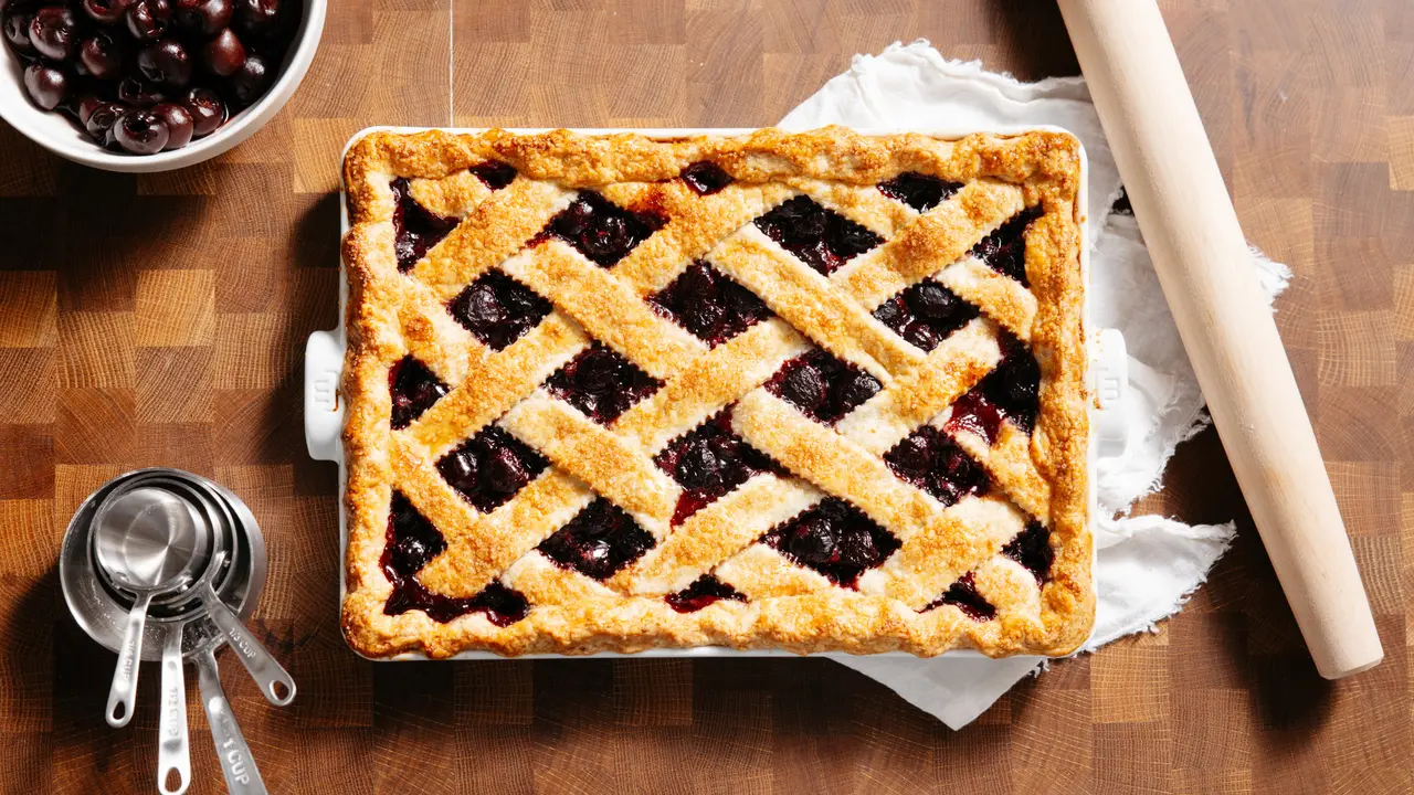 Made In Cherry Lattice Slab Pie with a golden crust and dark cherries rests on a wooden board.