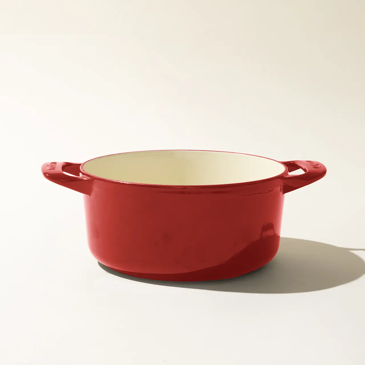 A red enameled cast iron Dutch oven with handles on a neutral background.
