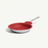 A red frying pan with a silver handle is displayed against a plain background.