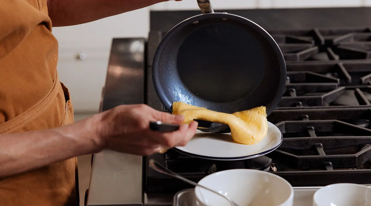 A person is flipping a crepe onto a plate from a pan in a kitchen setting.
