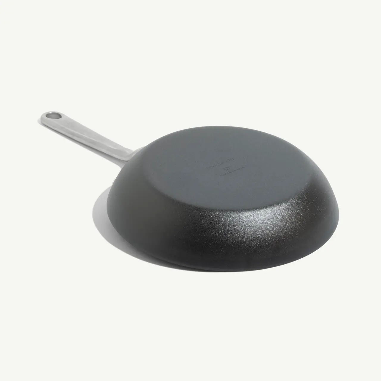 A black frying pan with a stainless steel handle is shown upside down against a neutral background.