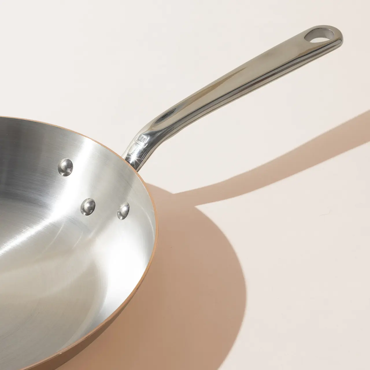A stainless steel frying pan casting a shadow on a light surface.