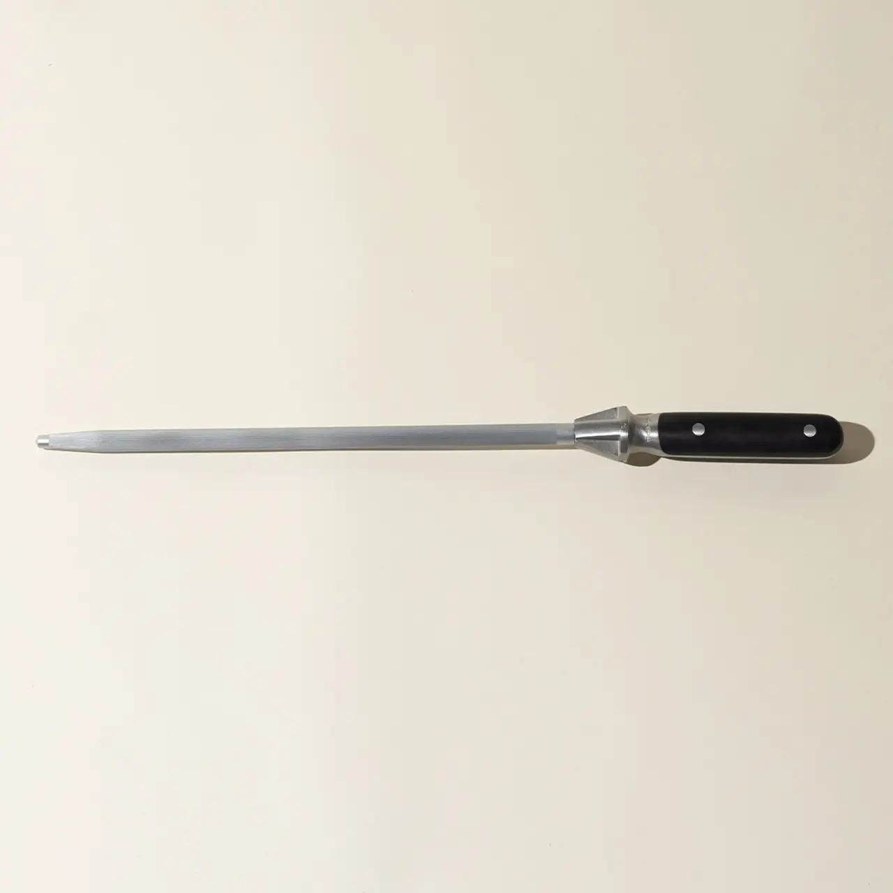 A long steel honing rod with a black handle lies against a neutral background.
