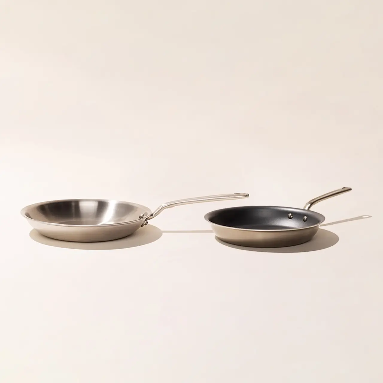 Two frying pans, one stainless steel and one with a non-stick surface, are placed side by side against a neutral background.