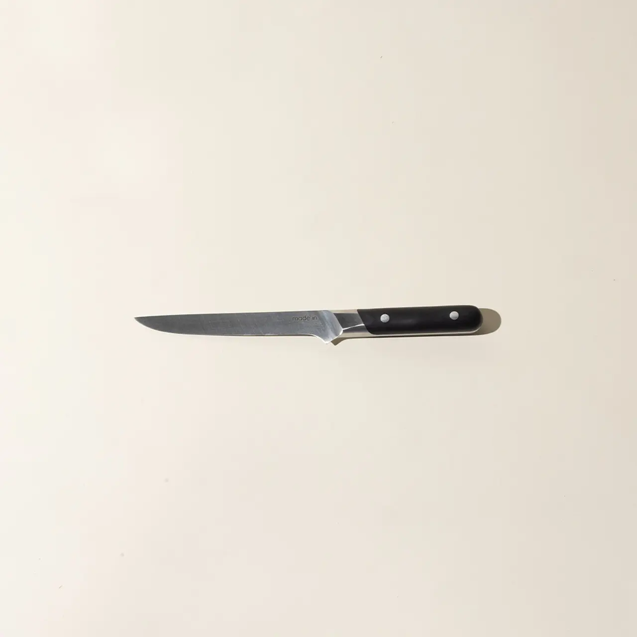 A single kitchen knife with a black handle is centered on a plain light-colored background.