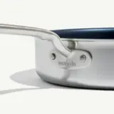 A close-up of a stainless steel pan with the text "made in" etched near the handle, casting a shadow on a light surface.