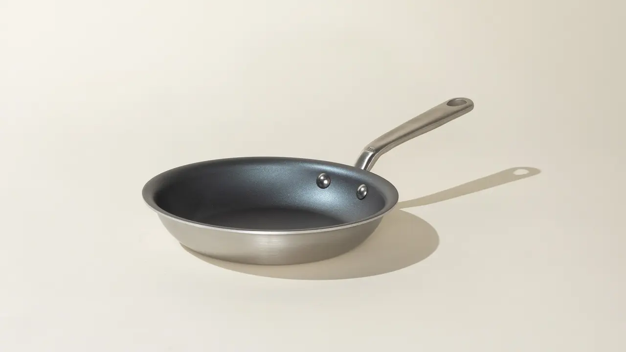 A non-stick frying pan with a silver exterior and black interior sits on a neutral background.