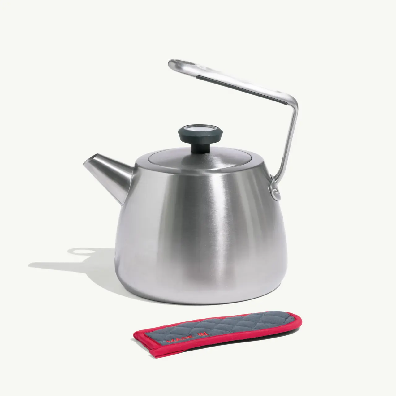 A sleek stainless steel kettle is positioned next to a red and black heat-resistant pot holder.